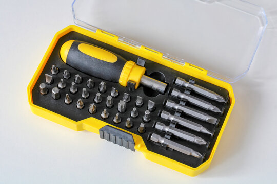 A open yellow plastic case containing a screwdriver handle and replaceable drill bits resting on a white background.