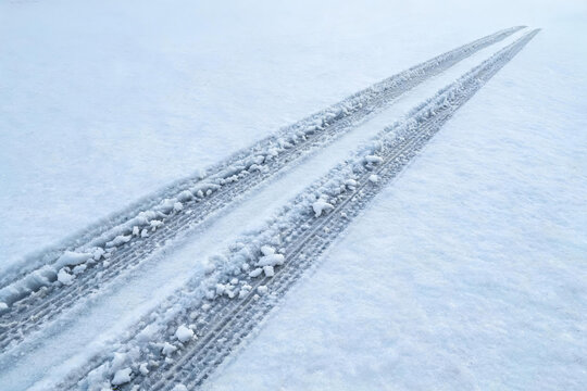 Two parallel tire tracks pressed into fresh white snow, leading toward the distant horizon of a winter landscape.