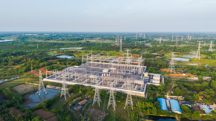 An aerial view of a large electrical substation with transmission towers, set in a green rural area with water bodies and vegetation. © tai