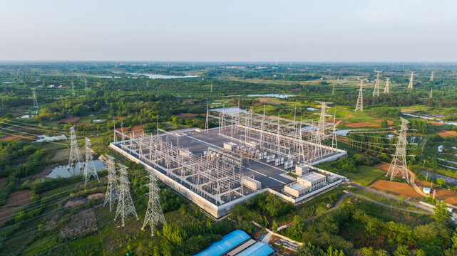 An aerial view of a large high-voltage electrical substation situated in a green rural area with surrounding natural landscapes.