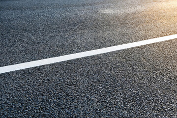 Fototapeta premium A close-up view of dark asphalt pavement with a crisp white traffic line marking, showing the rough texture of road material.