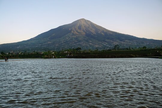 Majestic view of Mount Cikuray in Garut with a calm lake water surface in the afternoon.