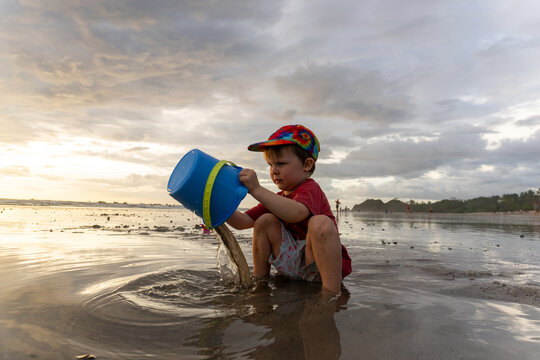 Young boy pouring water from bucket on a wet beach