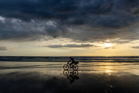 Man on a bicycle silhouetted on a beach at sunset