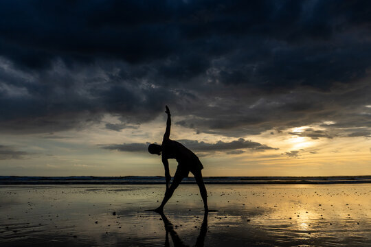 Person doing yoga on a wet beach at sunset