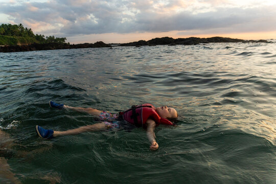 Boy in life jacket floating at sunset