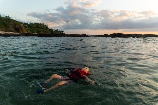Young child floating in the ocean at sunset