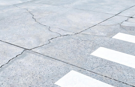 A section of weathered concrete pavement with visible cracks and white crosswalk markings for pedestrian use.