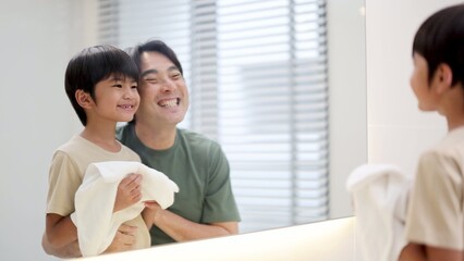 Obraz premium Asian Father and Son Laughing Together in Front of Bathroom Mirror