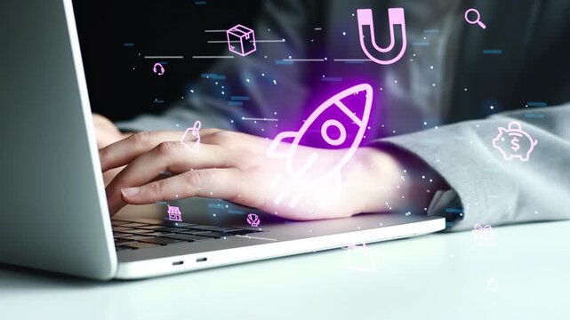 A person is typing on a laptop in an office setting. Digital icons are floating around, showing symbols like a rocket, a magnet, and a box. The scene takes place during the day.