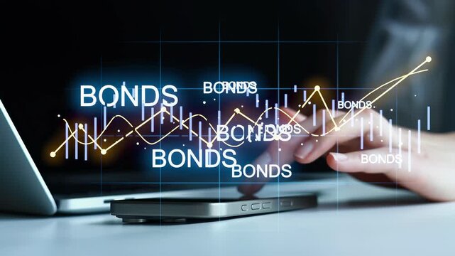 A person uses a laptop and smartphone to study bond market data. The screen shows graphs and information about bond trends. This happens indoors in a workspace setting.