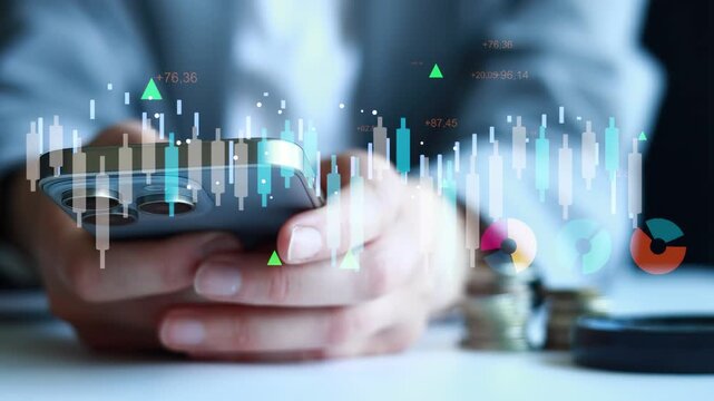 A person is looking at stock market data on a smartphone while seated at a table. There are coins nearby, showing an interest in finance. The focus is on the device and displayed information.