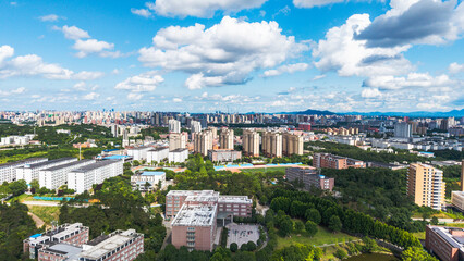 Naklejka premium A high-angle aerial shot of a campus area integrated with an urban city, surrounded by lush green trees under a bright blue sky.