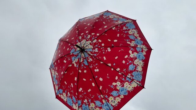 Bottom up view of a red floral umbrella open against a cloudy overcast sky during rainy weather.