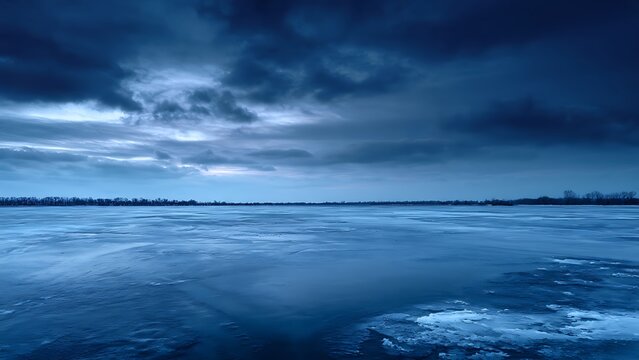 Dramatic moody winter landscape with frozen lake and dark stormy sky.