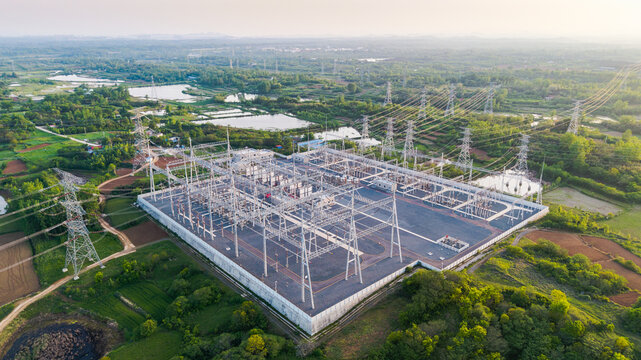 A large high-voltage power substation facility situated in a lush green rural area with transmission towers extending outward.