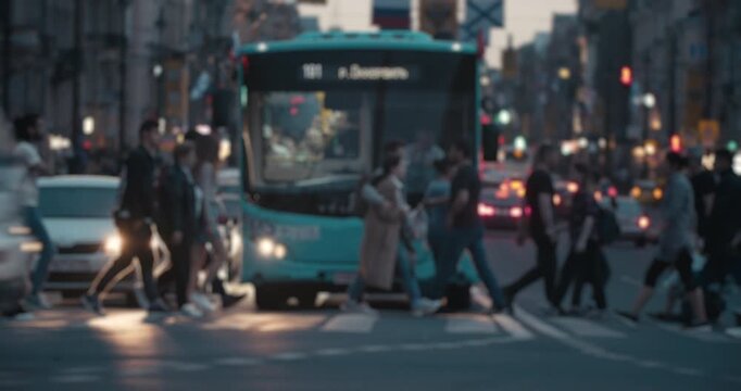 People crossing a city street in front of a public bus during busy evening traffic.
