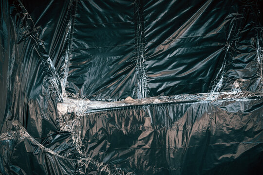 Dark, shiny polyethylene material background showing wrinkled, reflective surfaces and textured vertical lines.