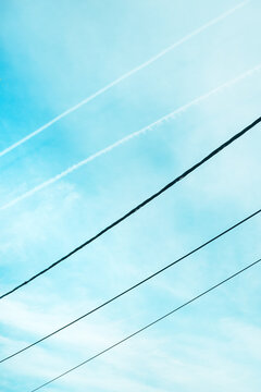 Minimal composition of a bright blue sky crossed by diagonal power lines and faint airplane contrails