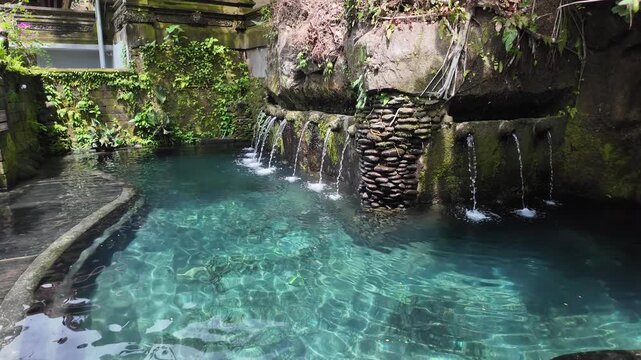 Clear natural spring pool with stone water spouts in Bali
