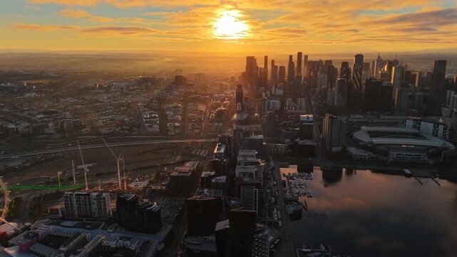 Aerial drone video of Melbourne CBD at sunrise, showing the northern city edge, Docklands, Marvel Stadium, waterways, cranes and golden light over the skyline