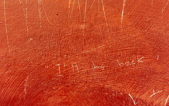 Mensaje grabado en una pared en ingl&eacute;s: "I'll be back". Pared roja con signos de desgaste y acabado tosco.
