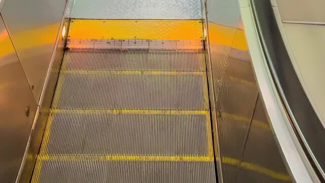 Escalator steps with yellow safety markings and metallic surface in urban transit environment