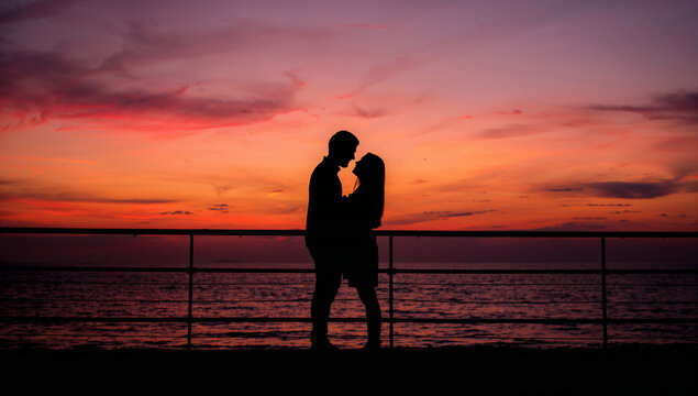 Romantic couple silhouetted against a vibrant sunset over the ocean