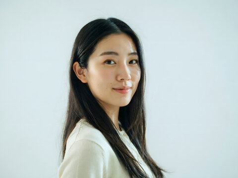 Portrait of a young east asian woman with long dark hair and natural makeup looking at the camera against a plain light gray background