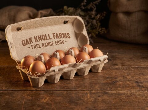 Brown free range eggs in a branded cardboard carton on a rustic wooden table with burlap sacks