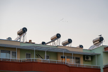 a row of cylindrical solar water heating systems mounted on the rooftop of a multi-story residential apartment building © Andrey