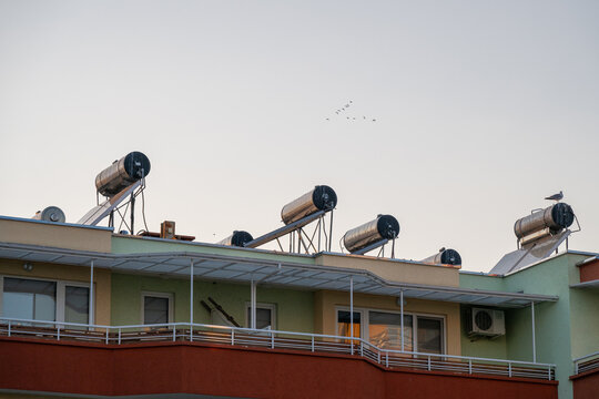 a row of cylindrical solar water heating systems mounted on the rooftop of a multi-story residential apartment building