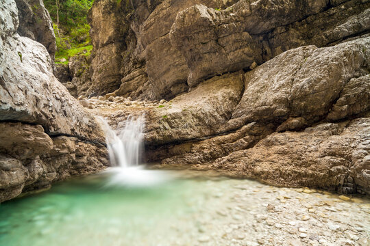 Waterfall cascading into a turquoise mountain pool in a rocky canyon, representing nature travel and tourism adventure, Julian Alps Natural Park, Resia, Friuli Venezia Giulia, Italy.