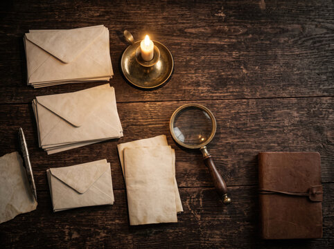Overhead view of mystery dinner party planning supplies with stacks of envelopes and blank paper on rustic wood
