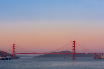 Obraz premium A beautiful sunset view of the iconic Golden Gate Bridge in San Francisco, California, USA, with a cargo ship sailing beneath it.