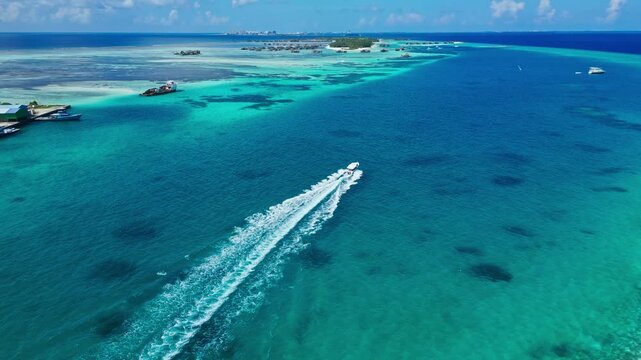 Boat speeding across the water, in maldives tropical reef with clear turquoise water, with boat, tropical islands, from a aerial view perspective, with blue, green accents, and sunny holiday mood.