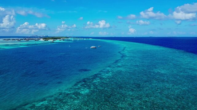 A serene aerial view of the Maldives, showcasing the tranquil tropical ocean and sky, with boats and a reef visible from a high-altitude perspective. The scene is bathed in sunlight, evocat.