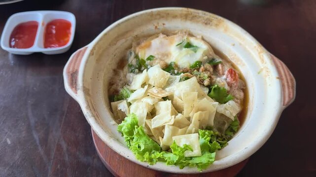 Delicious hot pot meal presented in a rustic earthenware dish with fresh green lettuce and a side of savory dipping sauces perfect for culinary blogs and food service establishments seeking