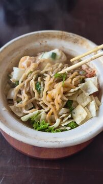 Delicious steaming bowl of savory noodles with fresh green vegetables and wontons seasoned with savory broth and served with wooden chopsticks for a satisfying meal capturing the essence of