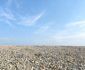 Obraz premium A vast expanse of smooth pebbles stretches to the horizon beneath a clear blue sky with wispy clouds.