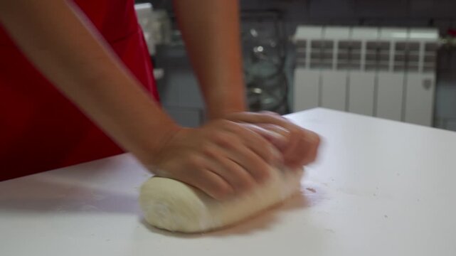 Skilled hands quickly roll and shape smooth bread dough on a white kitchen counter. This active domestic process creates a warm, satisfying feeling of joyful and energetic home baking.
