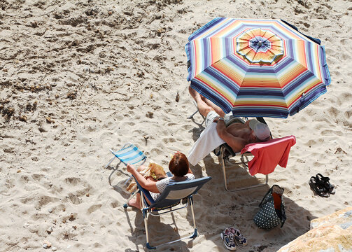 Pareja tomando el sol con combrilla, silla y hamaca en la arena de la playa en verano matrimonio tomando el sol en mar de vacaciones