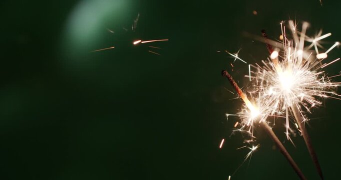 A single bright sparkler bursts with radiant white and golden sparks against a dark green-toned background.