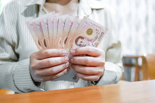 Woman holding Thai baht banknotes, representing finance, income, salary, savings, investment, money, cash, spending, personal budgeting, and everyday economic concepts, close-up