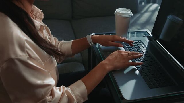 Woman working on laptop at home during daytime camera moves hands to face showing shift of focus from typing to face and concentrated workflow in home environment