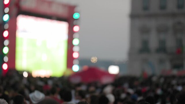Crowd of diverse football fans watching championship match on large screen in Lisbon, colorful lights illuminating the scene, excitement palpable in the evening atmosphere