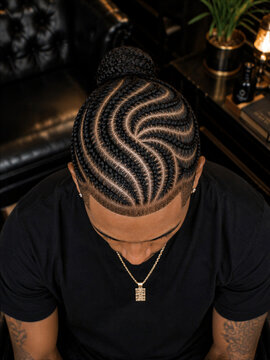 Man with intricate braided hairstyle sitting on a black leather couch