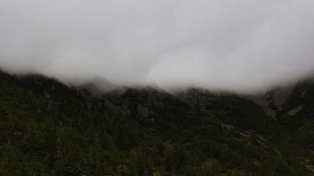 Dramatic time lapse of thick fog rolling over steep rocky ridges and pine forests on the way to Snezka mountain