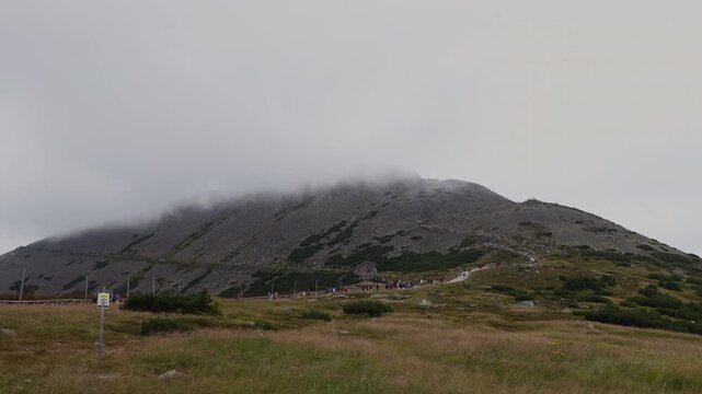 Timelapse of a large crowd of tourists hiking the trail to Snezka mountain peak under moving fog, Krkonose