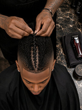 A stylist braiding a man's hair in a salon setting